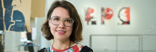 Header of happy young brunette female visitor of modern art gallery enjoying visiting vernissage and looking at camera