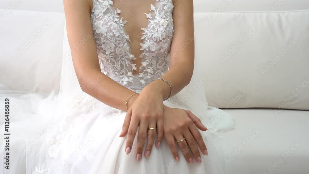 Elegant Bride in a Stunning Floral Lace Wedding Gown Sitting Gracefully on a White Sofa, Highlighting Sophisticated Jewelry and Perfectly Polished Nails for a Timeless Bridal Look Elegant Bride in a Stunning Floral Lace Wedding Gown Sitting Gracefully on a White Sofa, Highlighting Sophisticated Jewelry and Perfectly Polished Nails for a Timeless Bridal Look