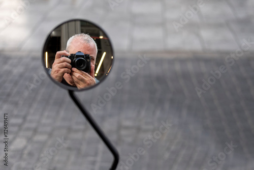Photographer taking a selfie reflected in a motorcycle mirror, copy space.