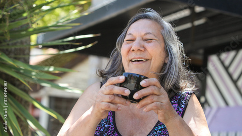 Fotografía cheerful senior latin woman drinking coffee or tea outdoors on sunny summer day