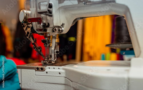 Close-up view of an industrial sewing machine with colorful fabrics and threads in the background. Perfect for themes related to fashion production, tailoring, and textile industry. photo