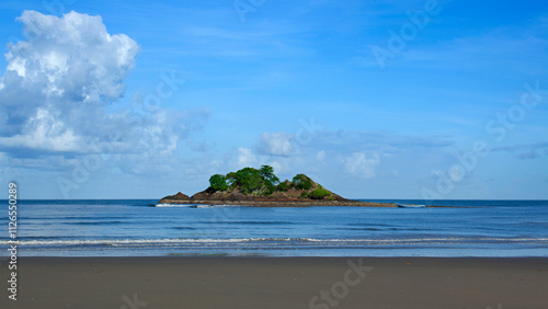 Ile rocher avec végétation tropicale avec une barque de pêcheur en bois dans une mer bleue en bord de plage au sable fin et sombre sous un ciel bleu et nuageux sur la côte est de l'Australie.