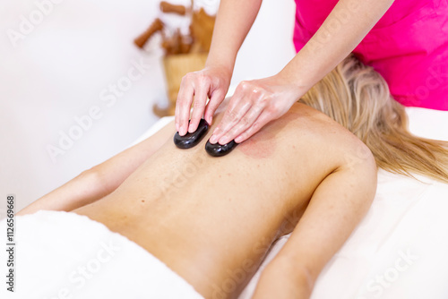 Hot stone massage therapy with smooth black stones being applied to a client's back. Ideal for concepts related to wellness, relaxation, spa treatments, and alternative therapies. photo