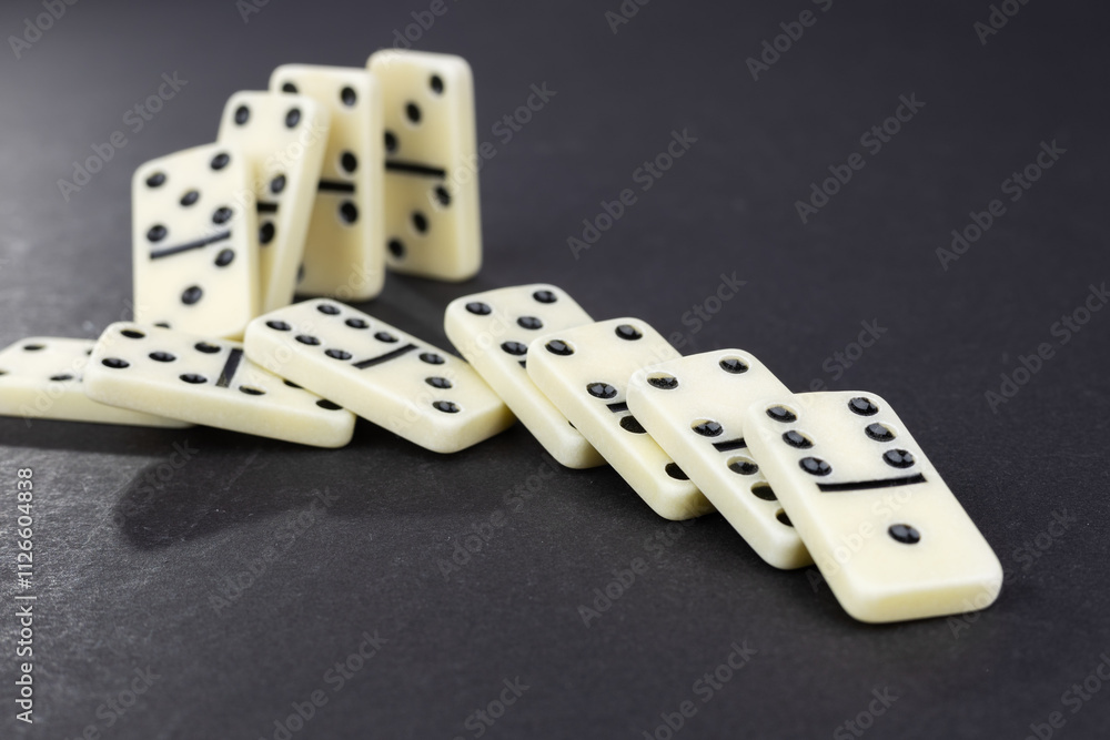 Domino effect concept with white dominoes pieces row falling on dark background. Domino effect concept with white dominoes pieces row falling on dark background.