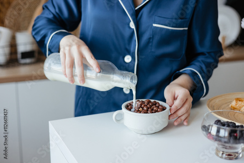 Beautiful girl pours cereal with milk in the kitchen