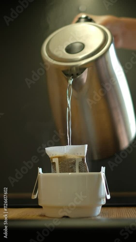 Modern coffee brewing: pouring hot water from an electric kettle into a drip bag over a white cup