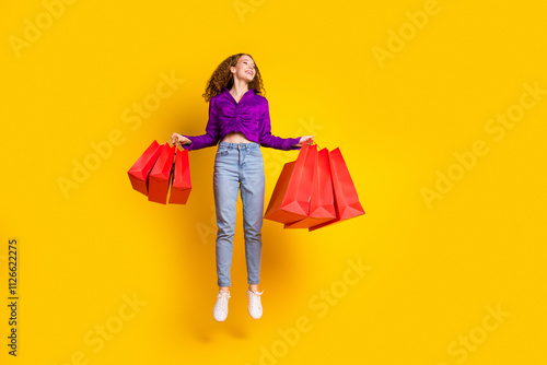 Full size photo of attractive young woman jump hold shopping bags dressed stylish violet clothes isolated on yellow color background
