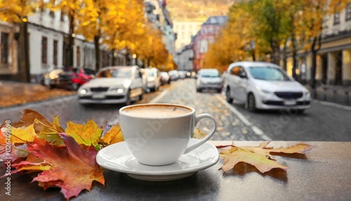 A Cozy Cup of Coffee on a Caf Table Surrounded by Vibrant Autumn Leaves and Street View with Cars in the Background Capturing the Essence of Fall in a Bustling Urban Setting photo