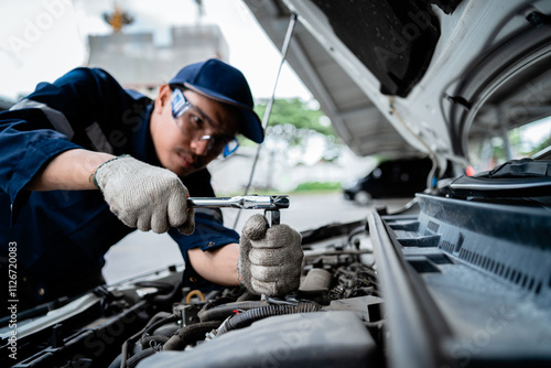 A mechanic is working on a car engine. The mechanic is wearing a blue shirt and a blue hat