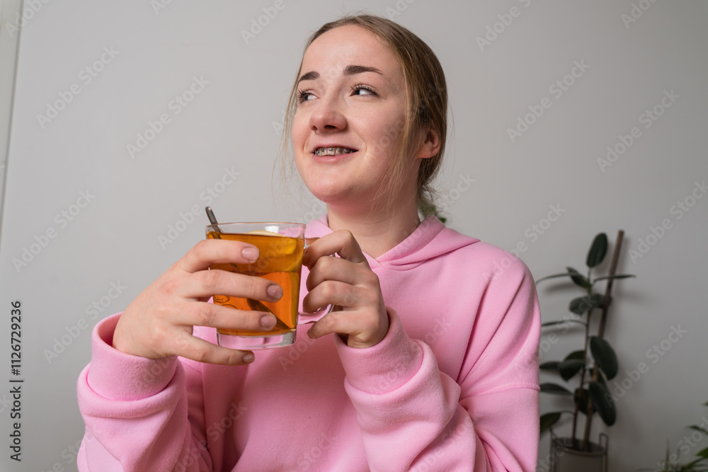Young girl with braces holds cup with tea at the kitchen Young girl with braces holds cup with tea at the kitchen