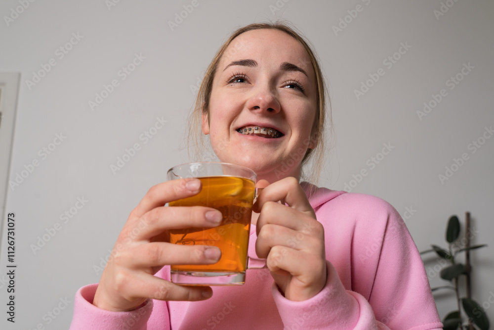 Young girl with braces holds cup with tea at the kitchen Young girl with braces holds cup with tea at the kitchen