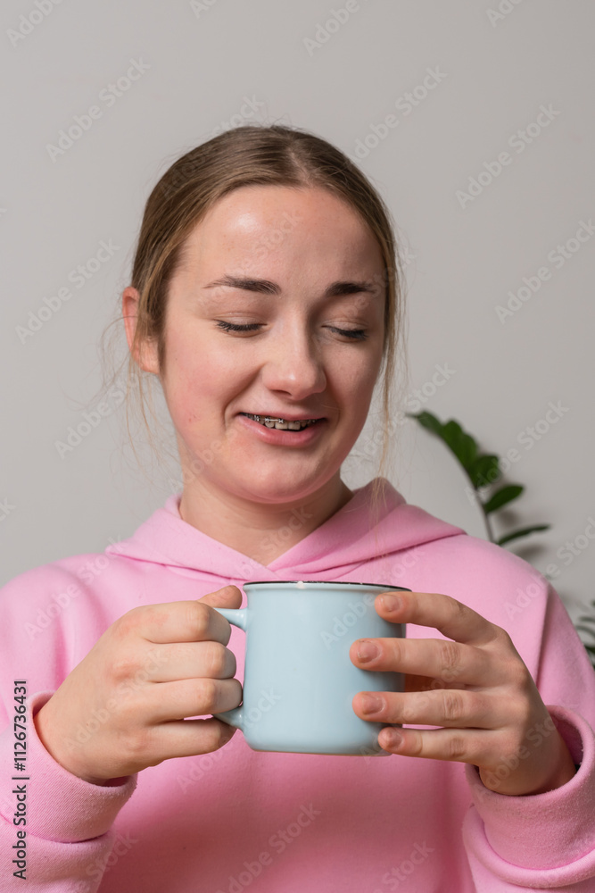 Young girl with braces holds cup with tea at the kitchen Young girl with braces holds cup with tea at the kitchen