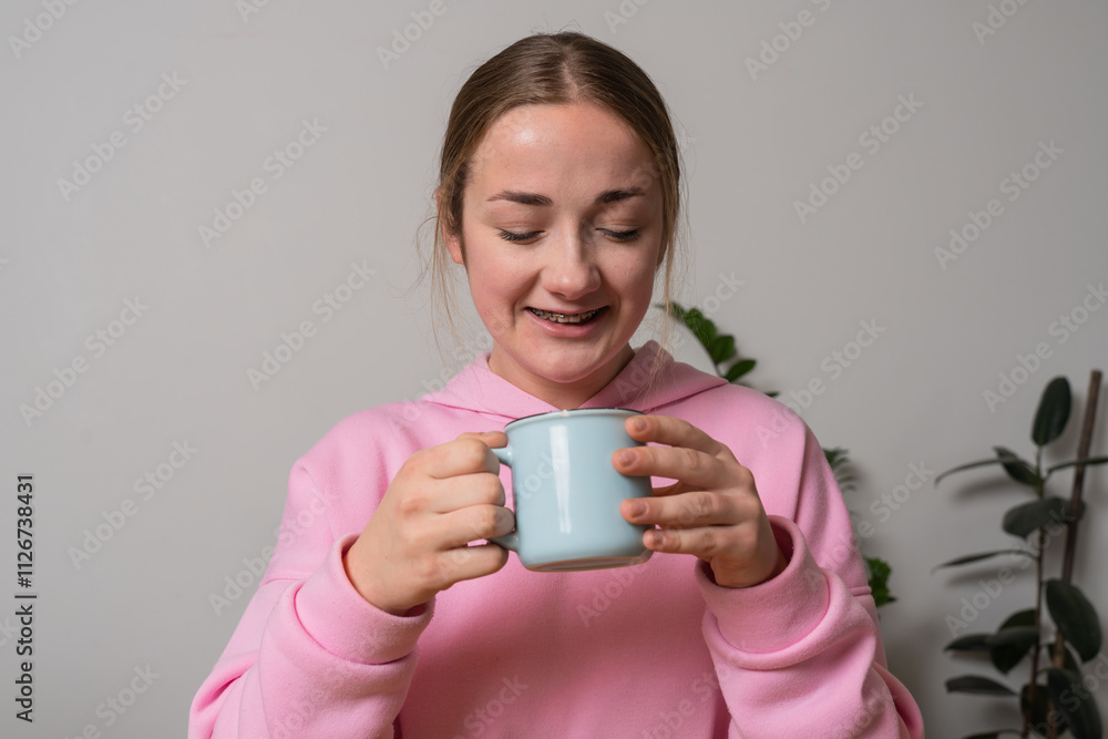 Young girl with braces holds cup with tea at the kitchen Young girl with braces holds cup with tea at the kitchen