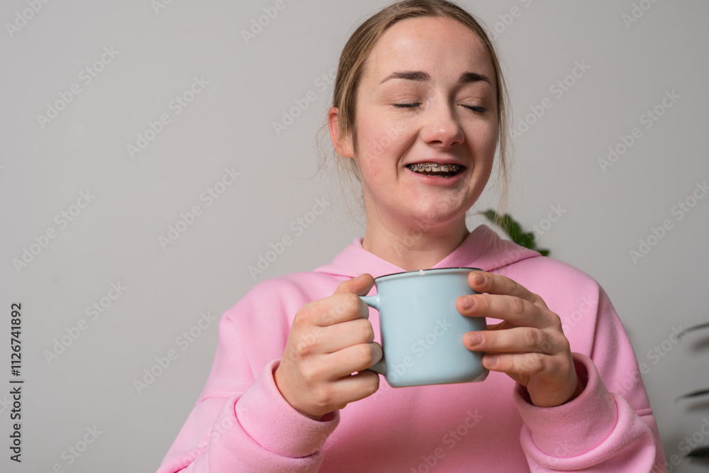 Young girl with braces holds cup with tea at the kitchen Young girl with braces holds cup with tea at the kitchen