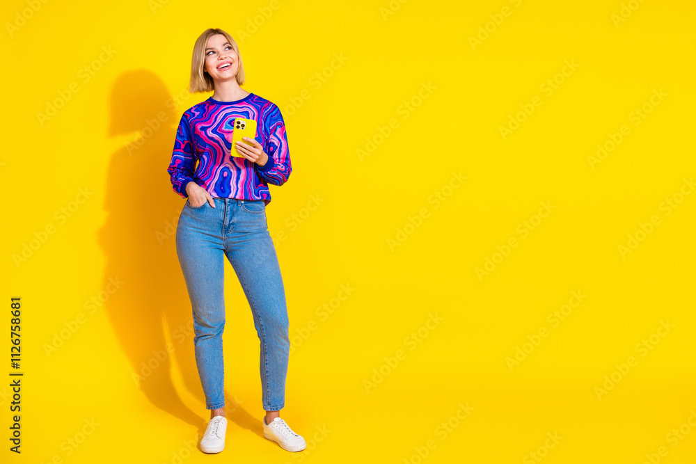 Full length photo of lovely young lady look empty space hold device dressed colorful blue garment isolated on yellow color background Full length photo of lovely young lady look empty space hold device dressed colorful blue garment isolated on yellow color background
