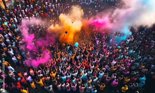 Aerial view of a large crowd of people celebrating a vibrant festival, throwing colorful powder in the air.