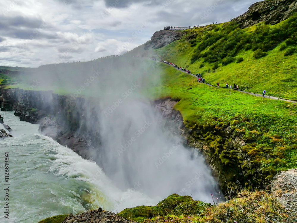 Panoramic view of Gullfoss falls and tourists walking by Panoramic view of Gullfoss falls and tourists walking by