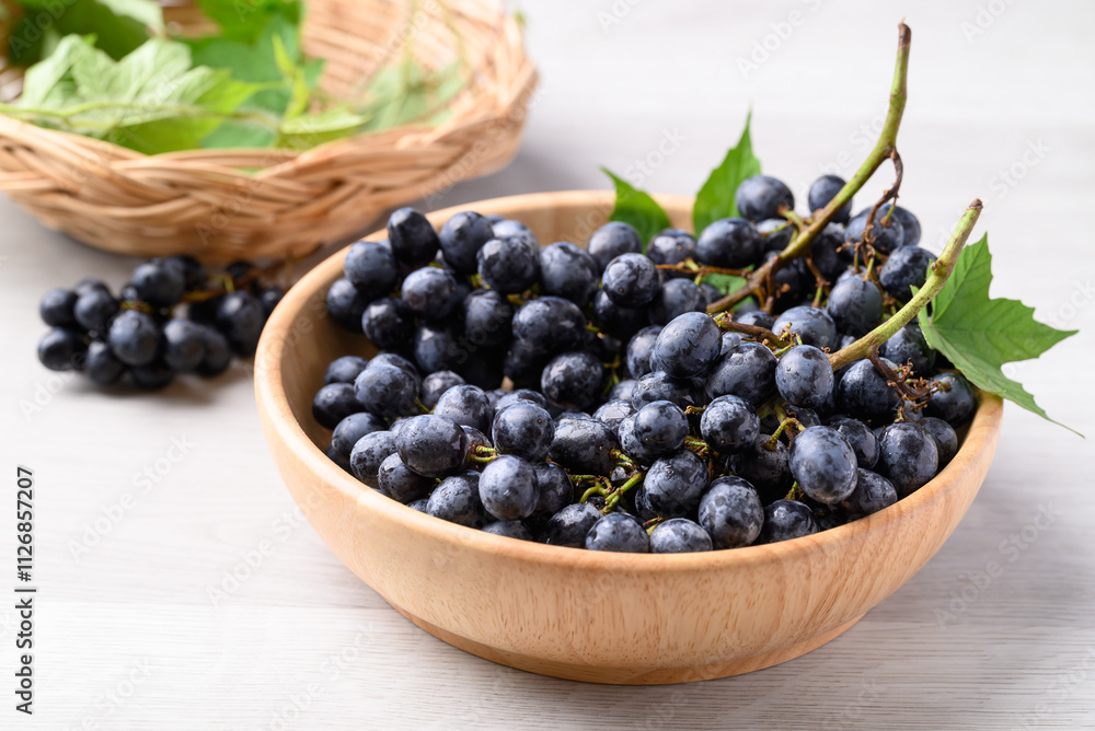Black grapes in wooden bowl on white table, Seedless grapes Black grapes in wooden bowl on white table, Seedless grapes