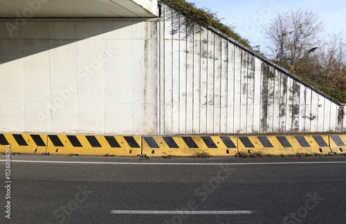 Exit of road tunnel. Concrete wall with yellow and black  cement guard rail on roadside.  Vegetation and sky on the right. Background for copy space.