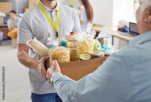 Volunteer working at charity center giving free food donations in cardboard box for mature man in charitable foundation. Humanitarian aid, volunteering and social help for poor concept. photo