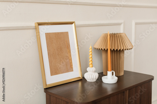 Empty wooden picture frame with two candlesticks and a lamp on a chest in a stylish living room photo