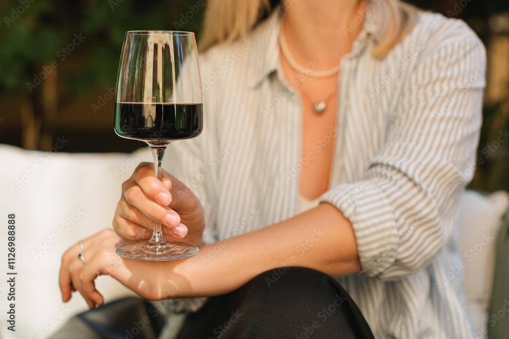 Close-up of a woman sitting on a terrace drinking a glass of red wine in summer Close-up of a woman sitting on a terrace drinking a glass of red wine in summer