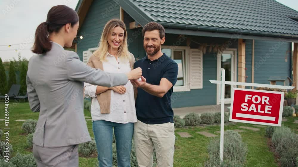 Real estate agent handing keys to beautiful building to charming Caucasian couple. Husband taking keys and smiling to his wife. People hugging each other. Happy about big purchase. Real estate agent handing keys to beautiful building to charming Caucasian couple. Husband taking keys and smiling to his wife. People hugging each other. Happy about big purchase.