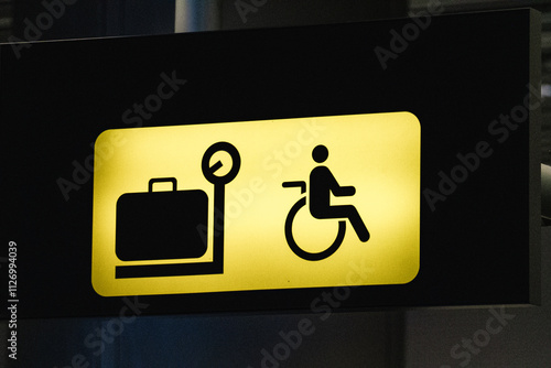 Yellow baggage claim sign with a luggage and wheelchair user symbol photo