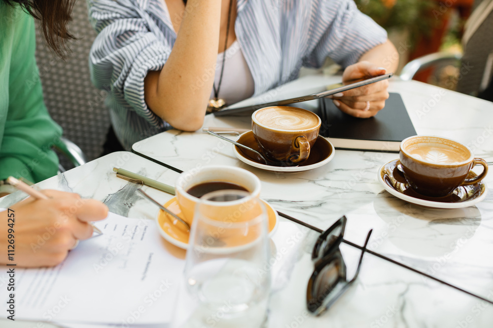 Two young women discussing work processes, signing documents and drinking coffee at a cafe Two young women discussing work processes, signing documents and drinking coffee at a cafe