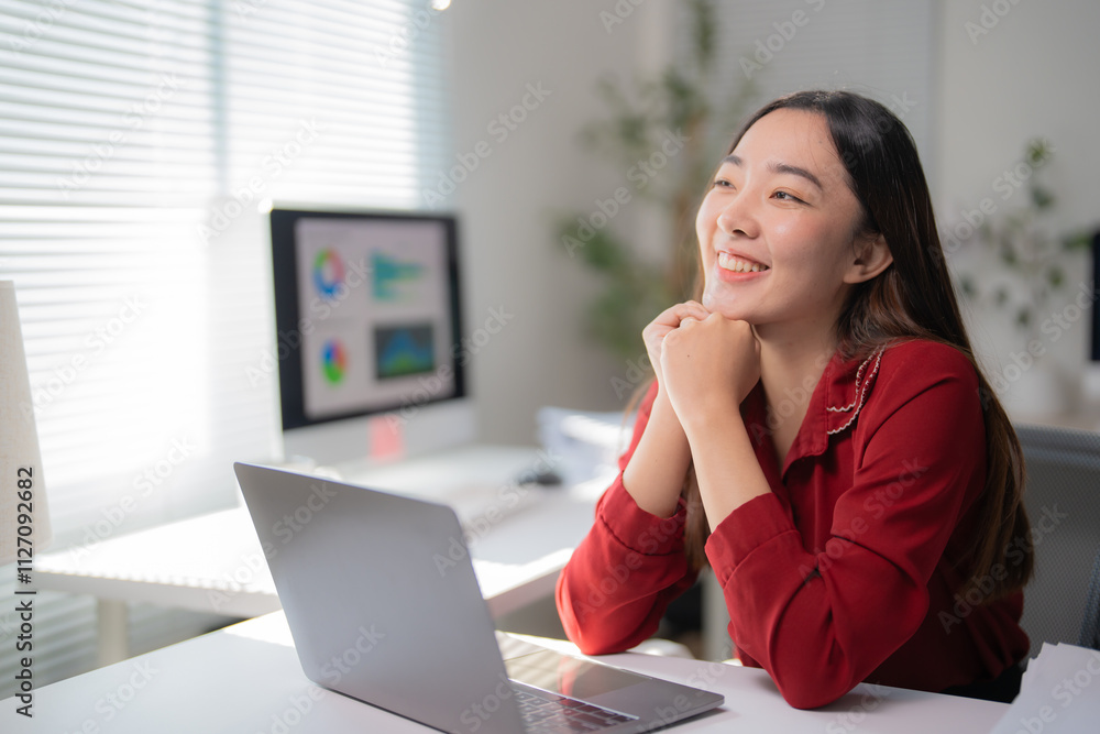 Happy business woman sitting at office desk, working on laptop computer, looking away and smiling, dreaming of future success, enjoying her work Happy business woman sitting at office desk, working on laptop computer, looking away and smiling, dreaming of future success, enjoying her work