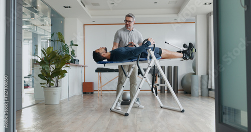 Physiotherapist, man and recovery on fitness bench with exercise, help and progress at clinic. People, biokinetics and support on table for rehabilitation process with injury treatment at hospital photo