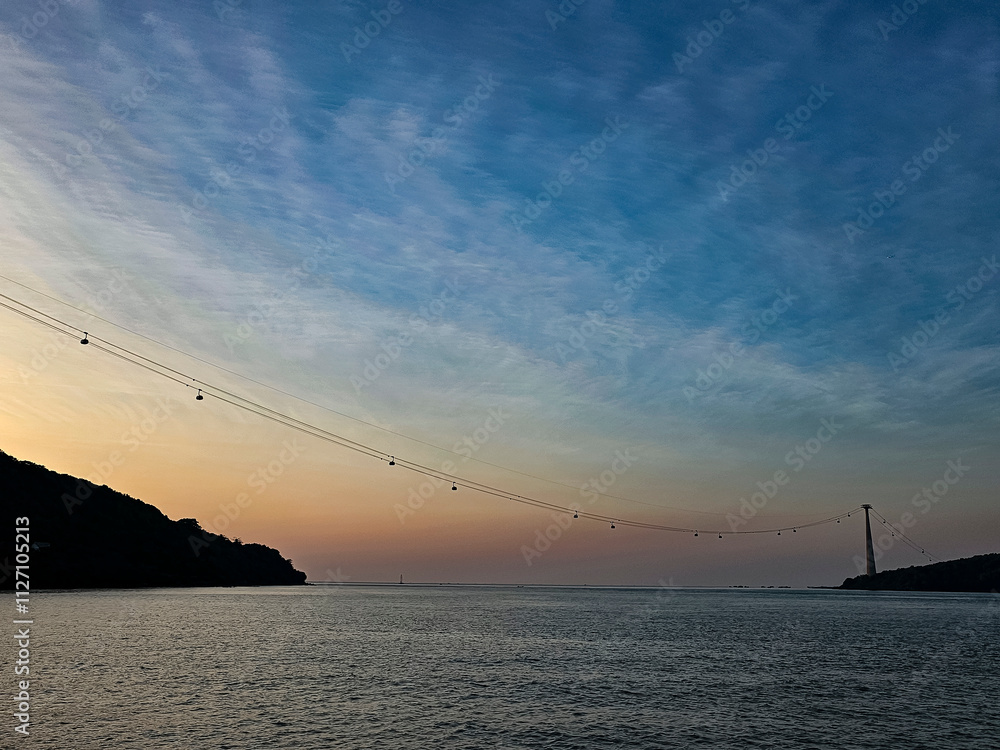 Fototapeta premium A beautiful sunset over the ocean with a bridge in the distance