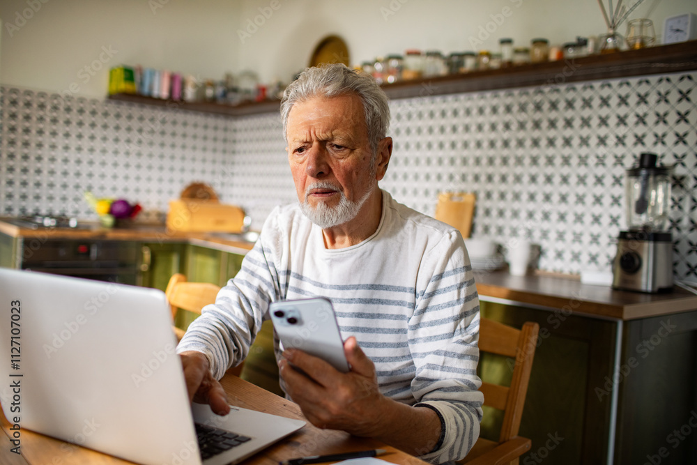 Stressed senior man reading bills on kitchen table with laptop Stressed senior man reading bills on kitchen table with laptop