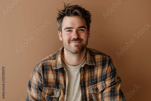 Portrait of a joyful man in his 30s wearing a comfy flannel shirt isolated on soft brown background