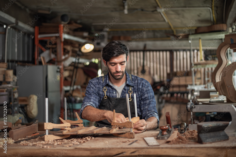 Luthier creating a guitar, clamps on the body of a guitar under construction improving glue adhesion Luthier creating a guitar, clamps on the body of a guitar under construction improving glue adhesion