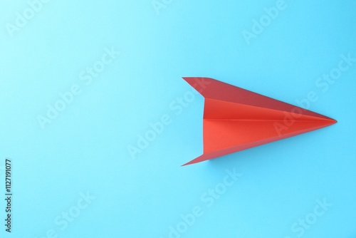 One handmade coral paper plane on light blue background, top view. Space for text