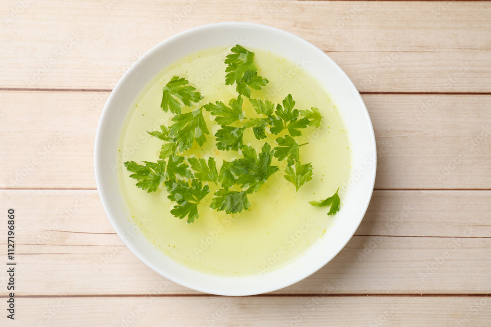 Tasty chicken bouillon with parsley in bowl on wooden table, top view Tasty chicken bouillon with parsley in bowl on wooden table, top view