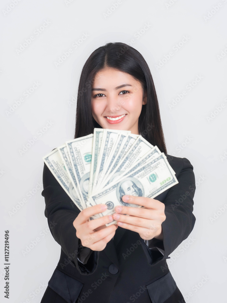 Confident young Asian businesswoman holding a fan of US dollar bills, smiling with success and financial achievement, dressed in a formal black suit against isolated on white background Confident young Asian businesswoman holding a fan of US dollar bills, smiling with success and financial achievement, dressed in a formal black suit against isolated on white background