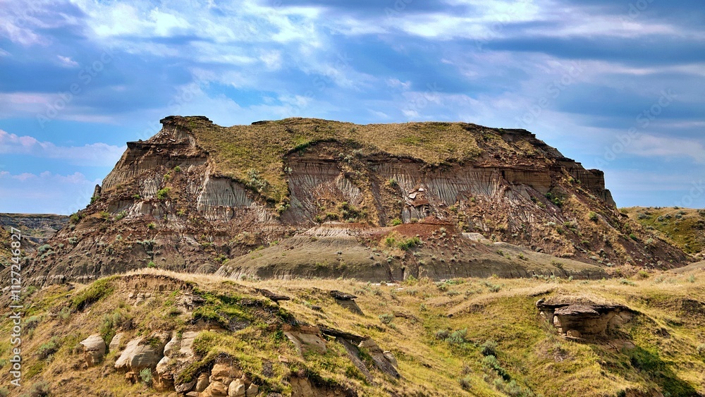 A stunning image of the rugged Badlands terrain featuring layered hills, eroded rock formations, and lush sagebrush vegetation under a vibrant blue sky. The dramatic geological features and golden gra A stunning image of the rugged Badlands terrain featuring layered hills, eroded rock formations, and lush sagebrush vegetation under a vibrant blue sky. The dramatic geological features and golden gra