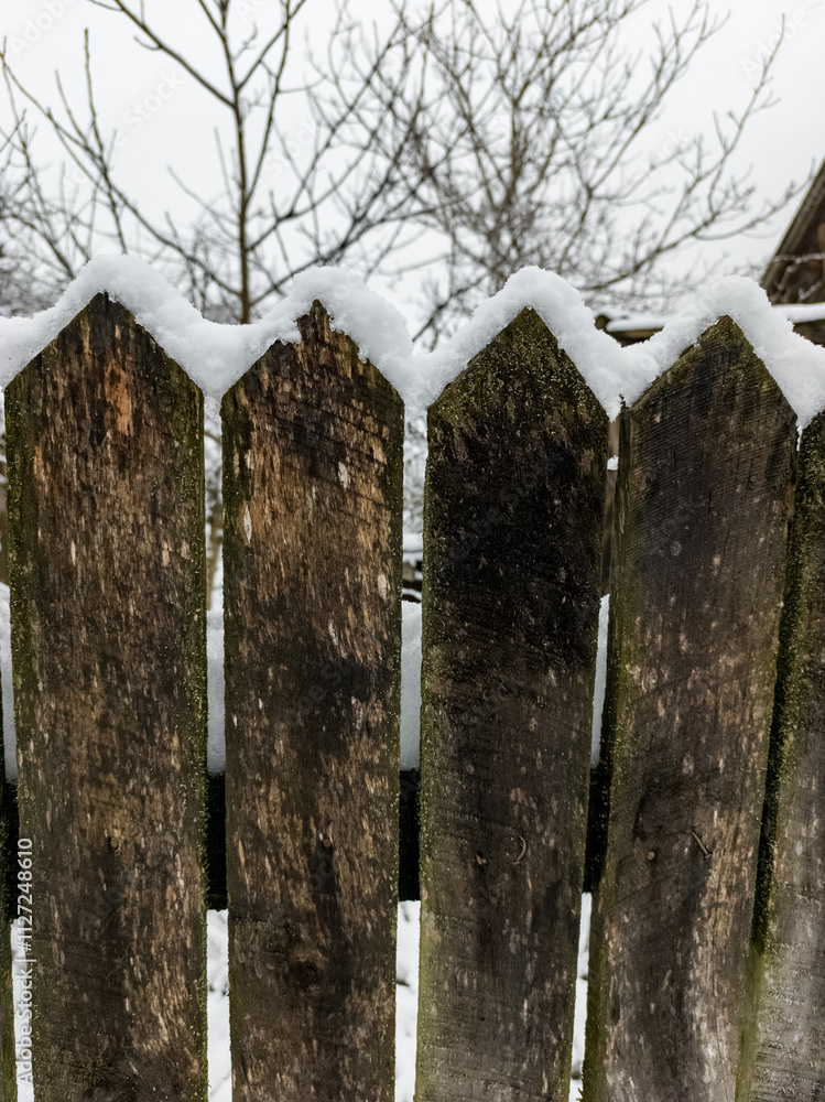 A wooden fence covered in snow next to a tree A wooden fence covered in snow next to a tree