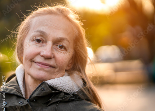 Old cheerful woman with a smiiley face walks in the city in the autumn sunny day.