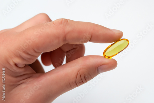 Obraz na płótnie Person holding yellow fish oil capsule. White capsule white background and fingers. Man with fish in his hands with white background and a fish in his hands. A man with a fish in a capsule lifestyle. w salonie