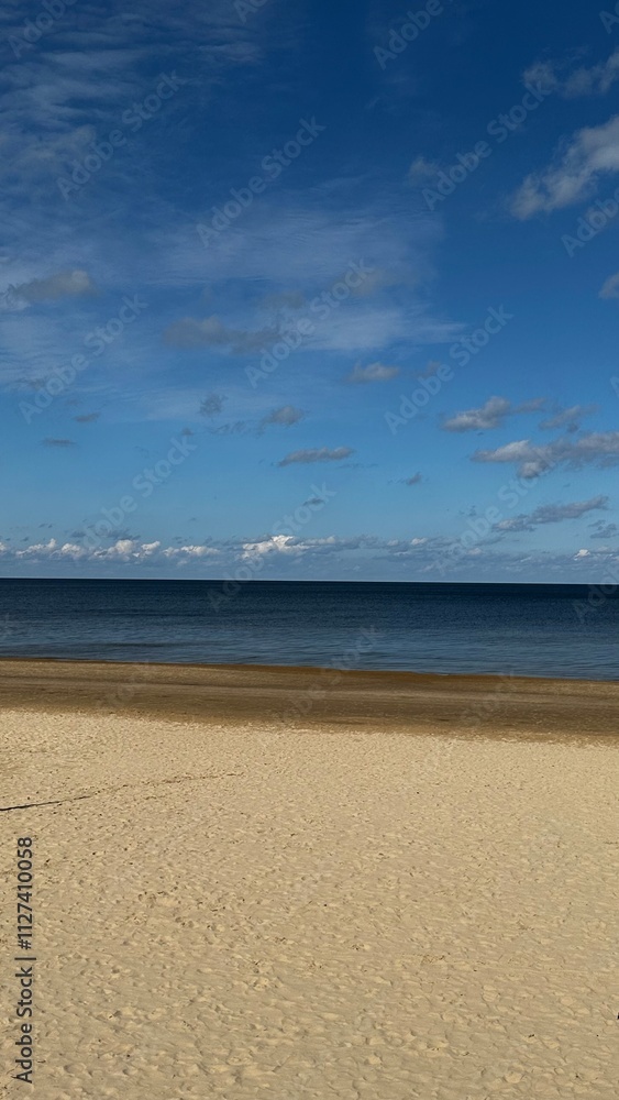 Obraz premium Serene sandy beach meets the calm blue sea under a vibrant sky, creating a balanced 50/50 effect between sand and sky, perfect for tranquility and inspiration