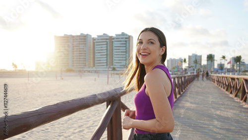 Panoramic banner view of beautiful smiling Brazilian girl turns around to the camera walking on pier at sunset on Aracaju beach, Sergipe, Brazil