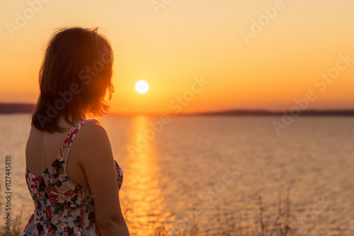 Woman standing in front of lake at sunset. Girl in blue sky at sunset. A sunset over the river and nature. A girl in a blue dress and blue skirt and a blue sky at lifestyle sunset in nature.