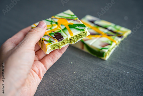 Piece of trend Dubai white chocolate with pistachio paste and kataifi dough in woman hand. Confectionery handmade sweets at home in the kitchen.  photo