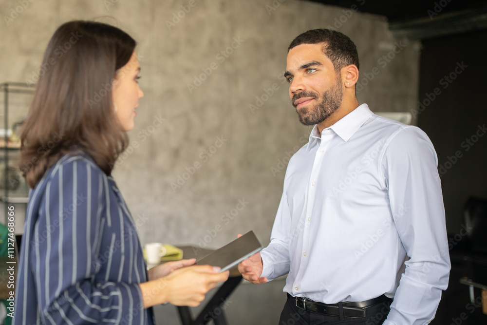 Obraz premium Two professionals engage in a productive discussion at a modern office. They exchange ideas and materials in a collaborative atmosphere, exemplifying teamwork and cooperation in their careers.