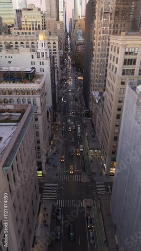 Vertical screen panning up reveals Fifth Avenue in Midtown Manhattan, New York City. Cars traverse street below and sun sets, casting a warm glow over the urban landscape photo