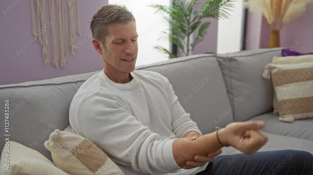Young man adjusting bracelet while sitting on a comfortable sofa in a stylish living room. Young man adjusting bracelet while sitting on a comfortable sofa in a stylish living room.