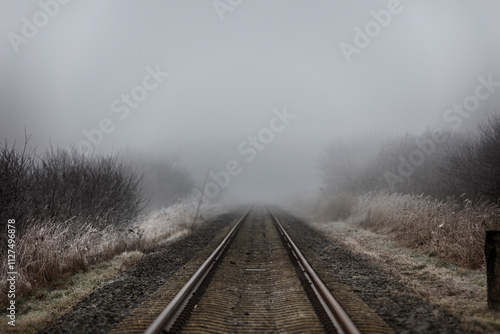 Fog-shrouded railway tracks wind through frosted fields.  A muted, winter scene.